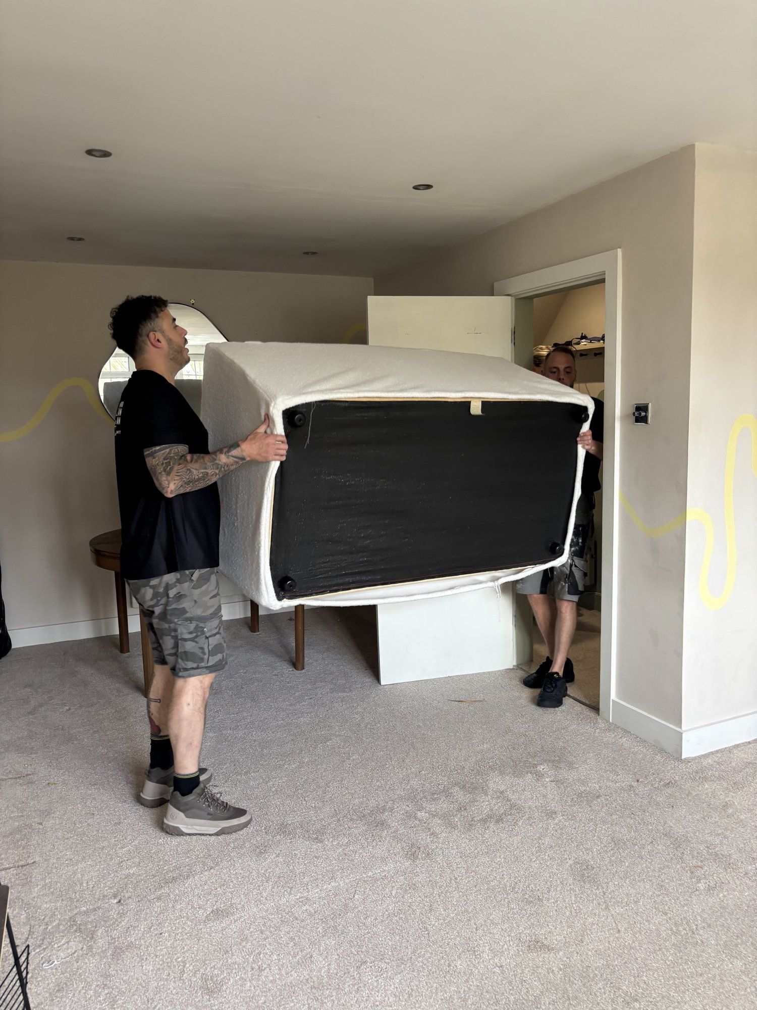 Two crew carrying an upholstered bed base through a bedroom doorway